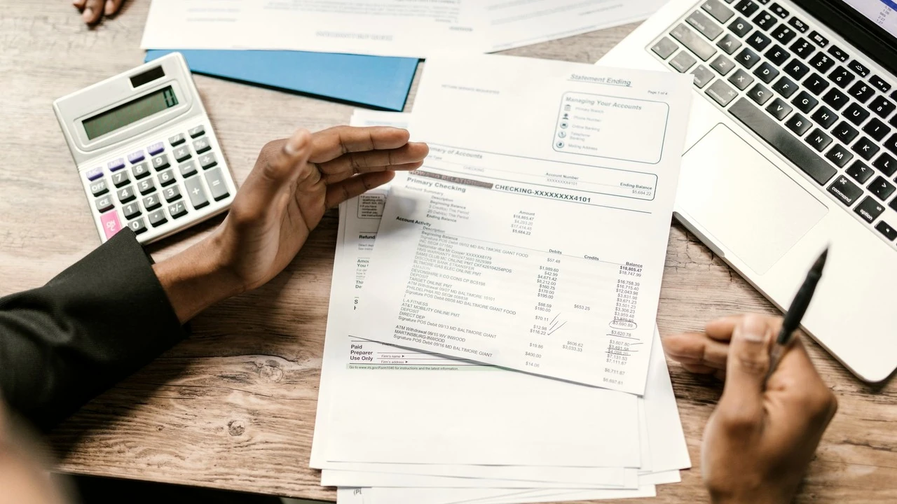Hands holding a printed statement next to a calculator and a laptop on an office desk