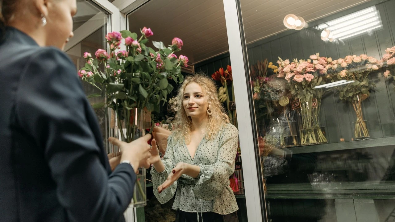 Una fiorista porge un mazzo di rose rosa a una cliente nel suo negozio di fiori